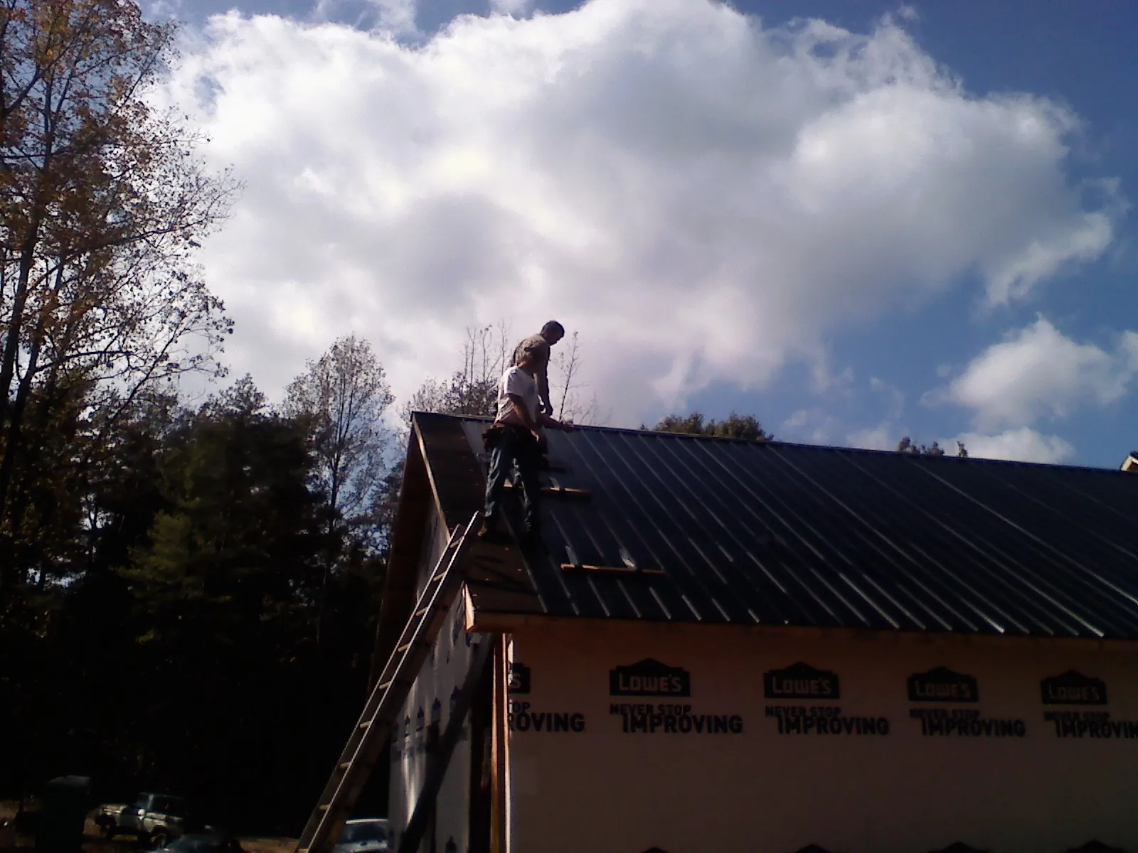 Roofer fastening dark metal panels high against a cloudy sky, from a Roof Inspection job in Dulzura